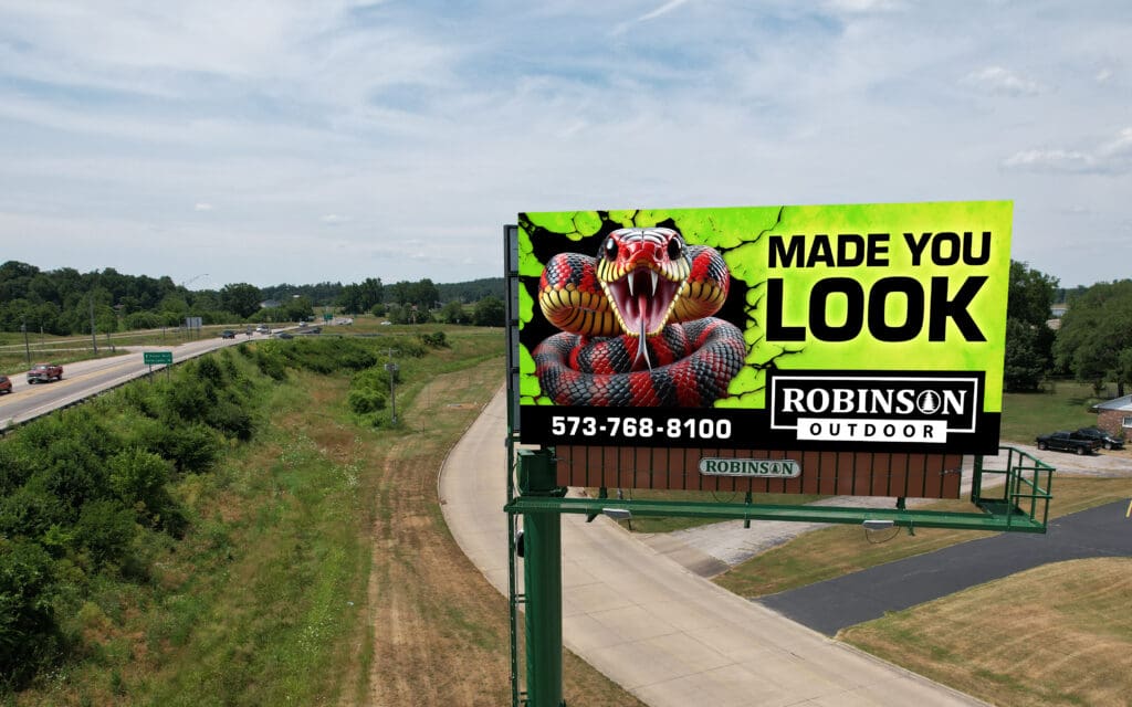 Billboard advertising a wildlife removal service with a raccoon image near a rural road.