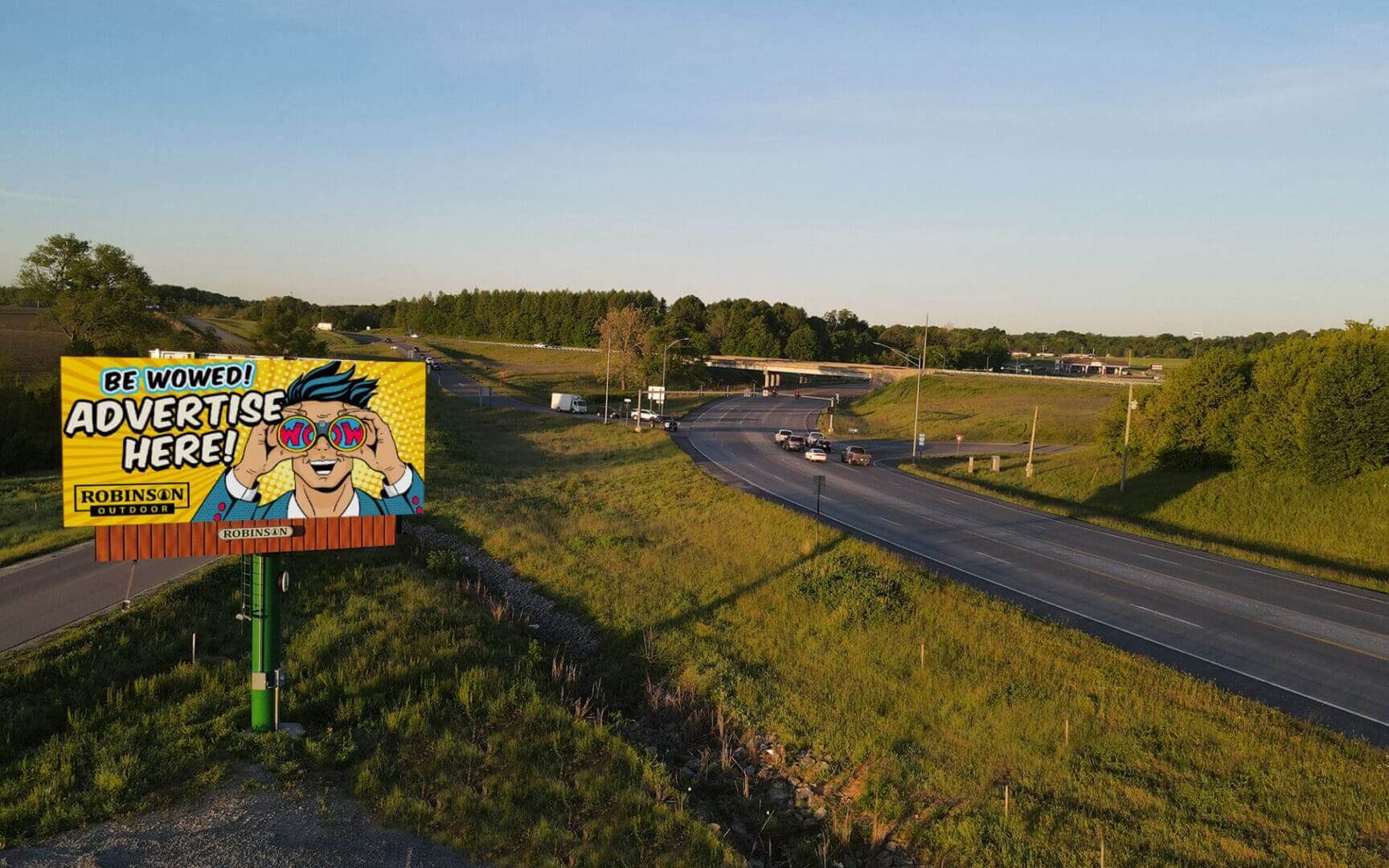 Road winding through a rural area with a colorful sign nearby under a clear sky.