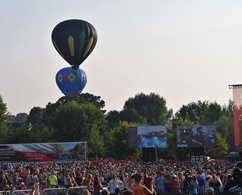 A crowd of people watching two balloons fly in the sky.