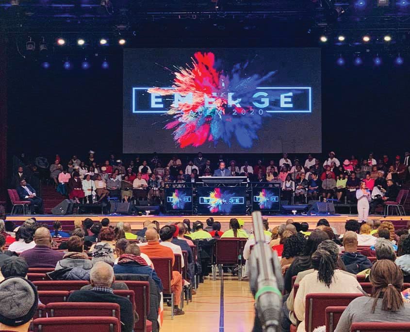 A large crowd of people sitting in front of a screen.