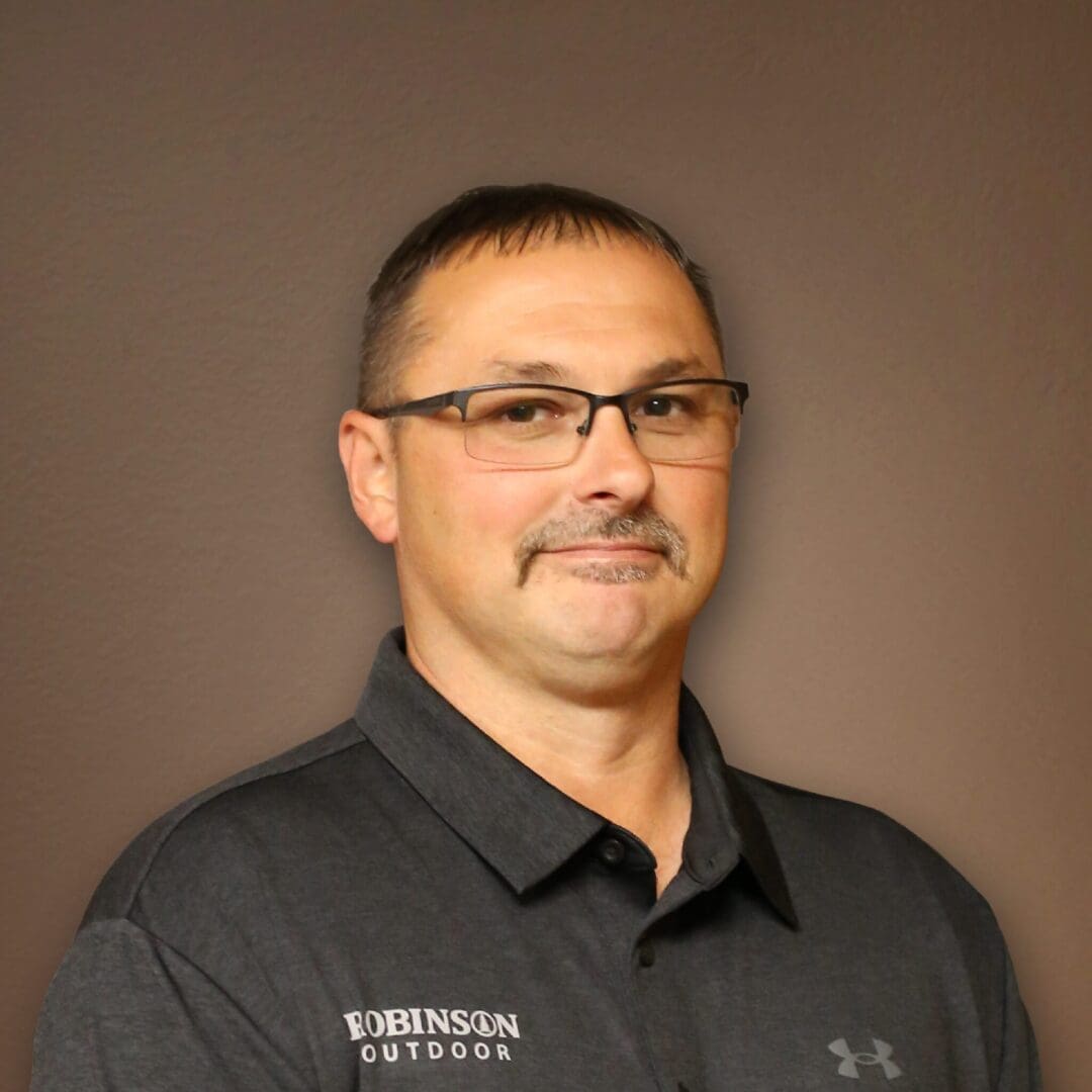 A man in glasses and black shirt standing next to wall.