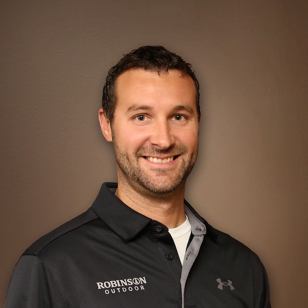Smiling man in a black Under Armour polo shirt against a brown backdrop.